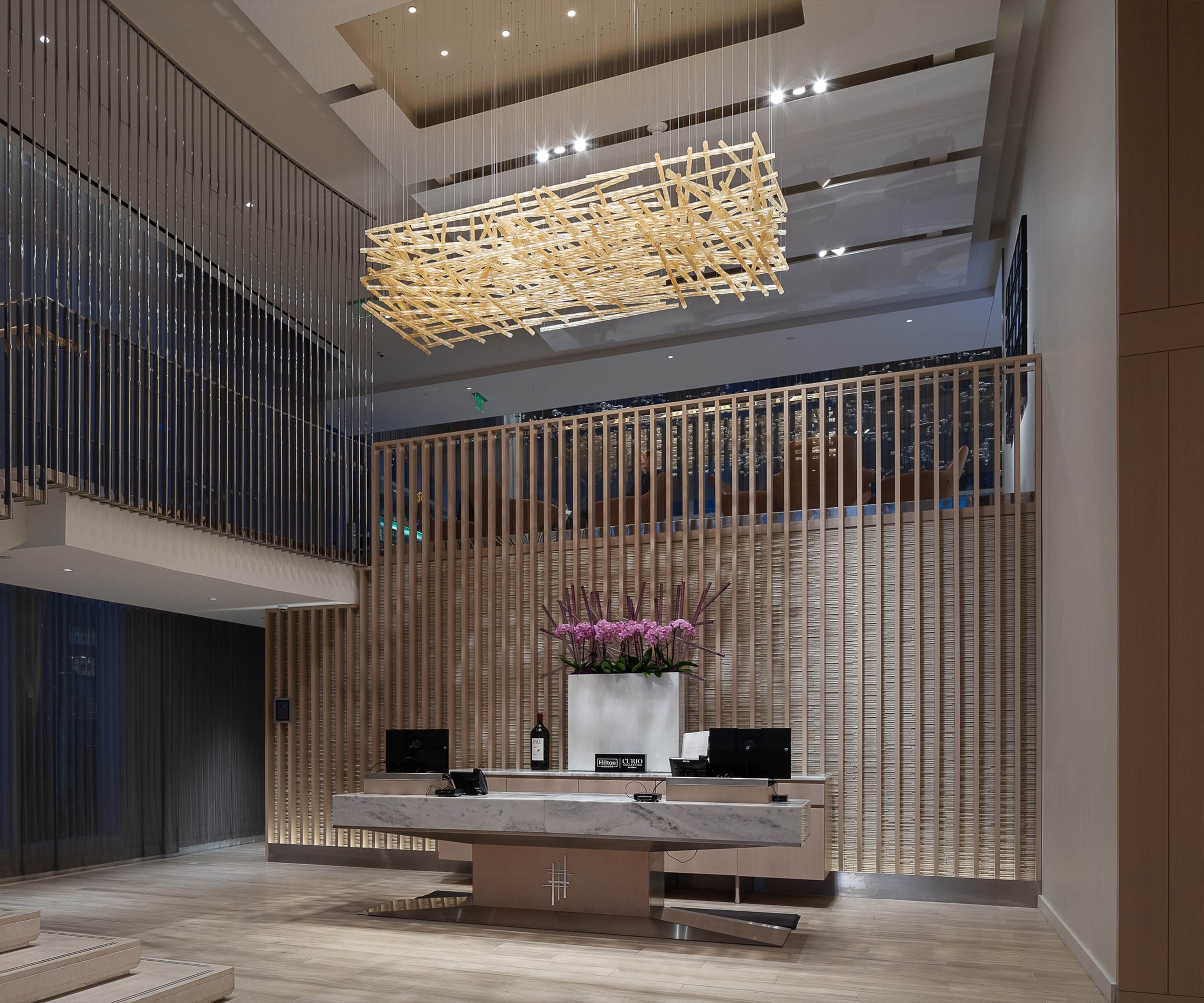 WOVEN glass chandelier by SHUCHUANG, gilded battens crossed over a reception desk