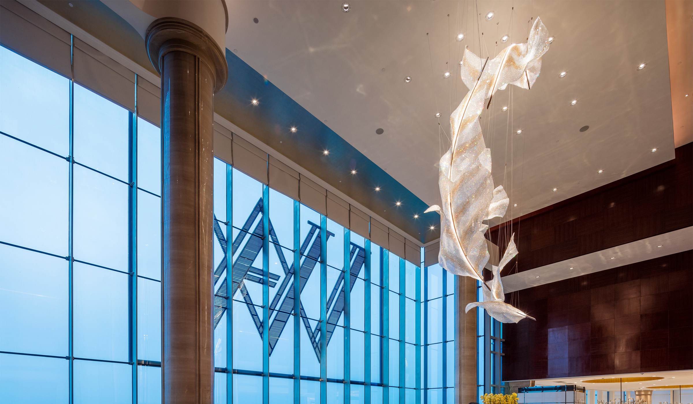 ARIA crystal feather chandelier by SHUCHUANG, seen against a full-height window wall