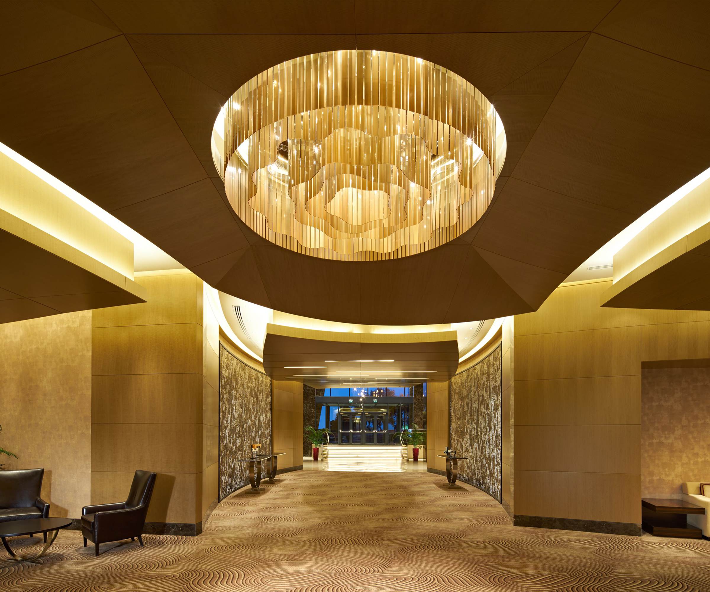 PAVILION gold chandelier set into a faceted ceiling recess above a hotel entrance